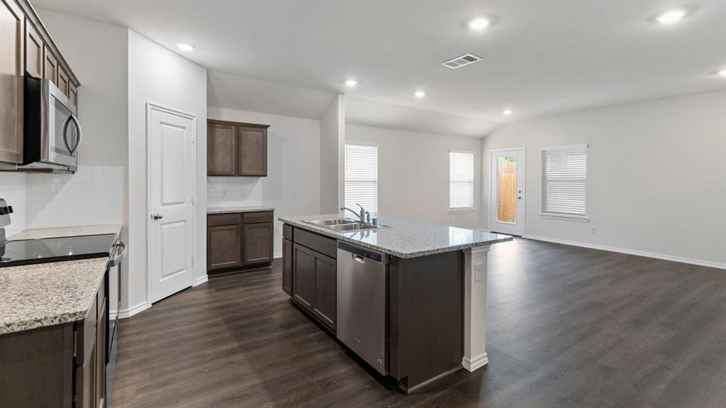 Kitchen island with integrated sink, stainless steel appliances, wood-finish flooring, recessed lighting, and granite countertops