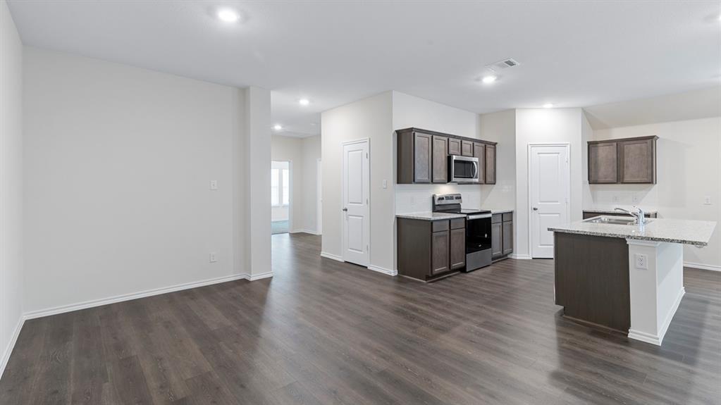 Expansive open-concept space featuring wood-finish flooring, recessed lighting, and a kitchen with dark cabinetry, stainless steel appliances, and a central island with a stone-finish countertop