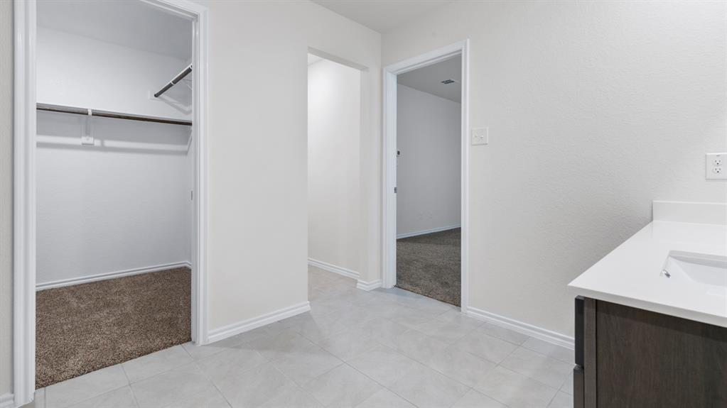 Tile flooring, light-toned walls, built-in closet shelving, dark wood-finish vanity, white countertop with integrated sink Tile flooring, light-toned walls, built-in closet shelving, dark wood-finish vanity, white countertop with integrated sink