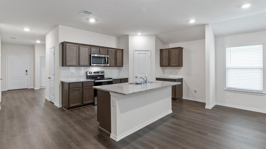 Kitchen featuring an island with a sink, stainless steel appliances, dark wood-finish cabinetry, and light-colored countertops