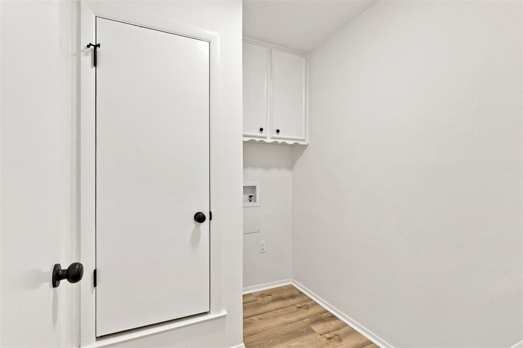 Built-in cabinetry with matte black hardware, wood-finish flooring, white walls, and a utility hookup