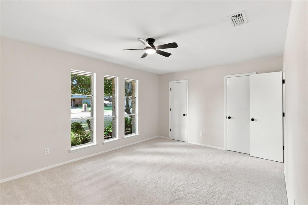 Carpeted room featuring multiple windows, a ceiling fan with light fixture, and closet doors