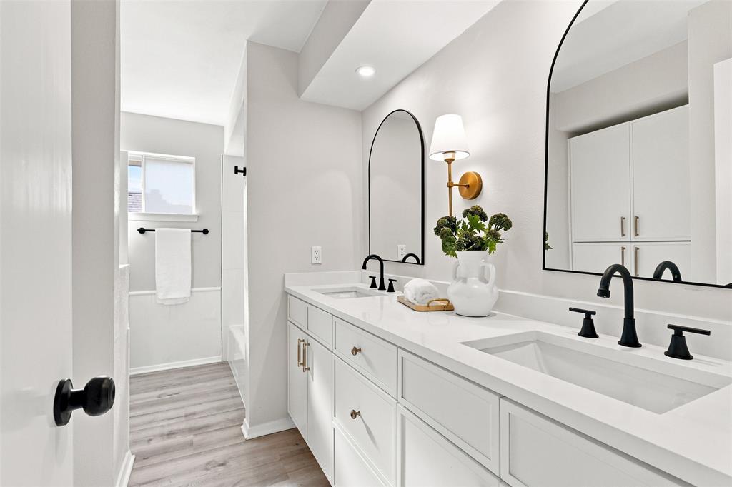 Dual vanity with integrated sinks, matte black fixtures, arched mirrors, built-in cabinetry, and wood-finish flooring