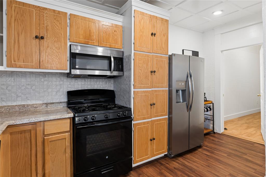 Wood-finish flooring with oak-finish cabinetry, stainless steel microwave, black range, and stainless steel refrigerator