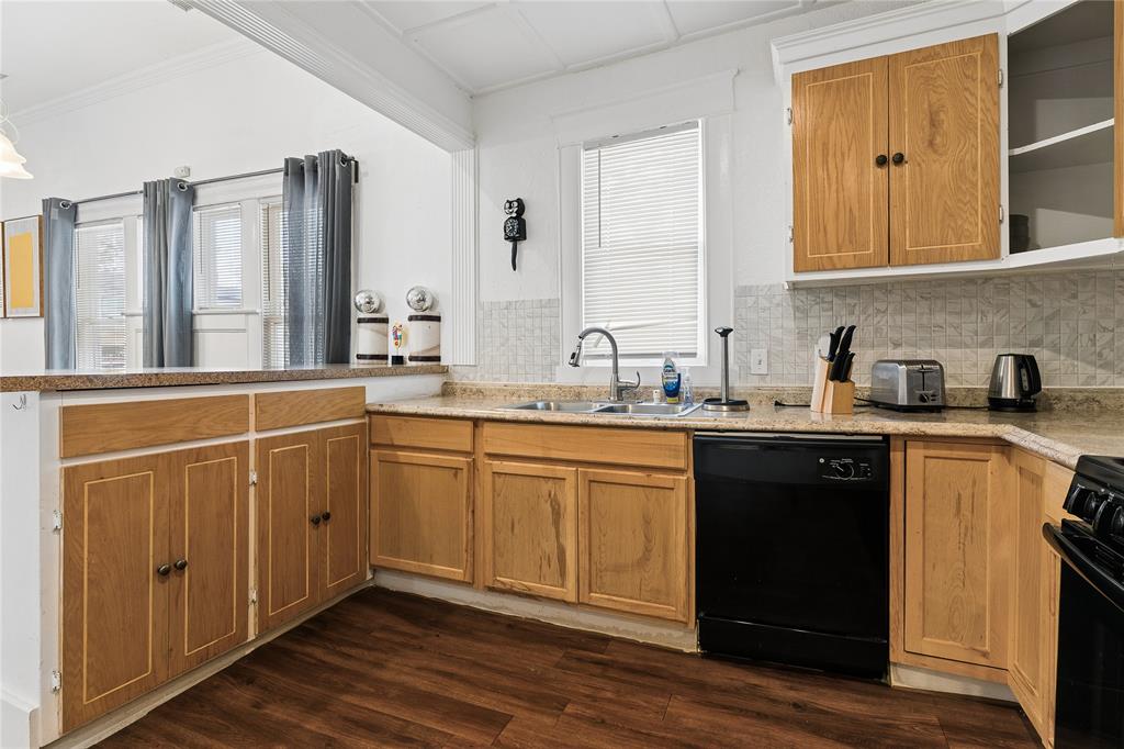 Wood-finish flooring, light wood cabinetry, stone-finish countertops, tile backsplash, and a stainless steel sink