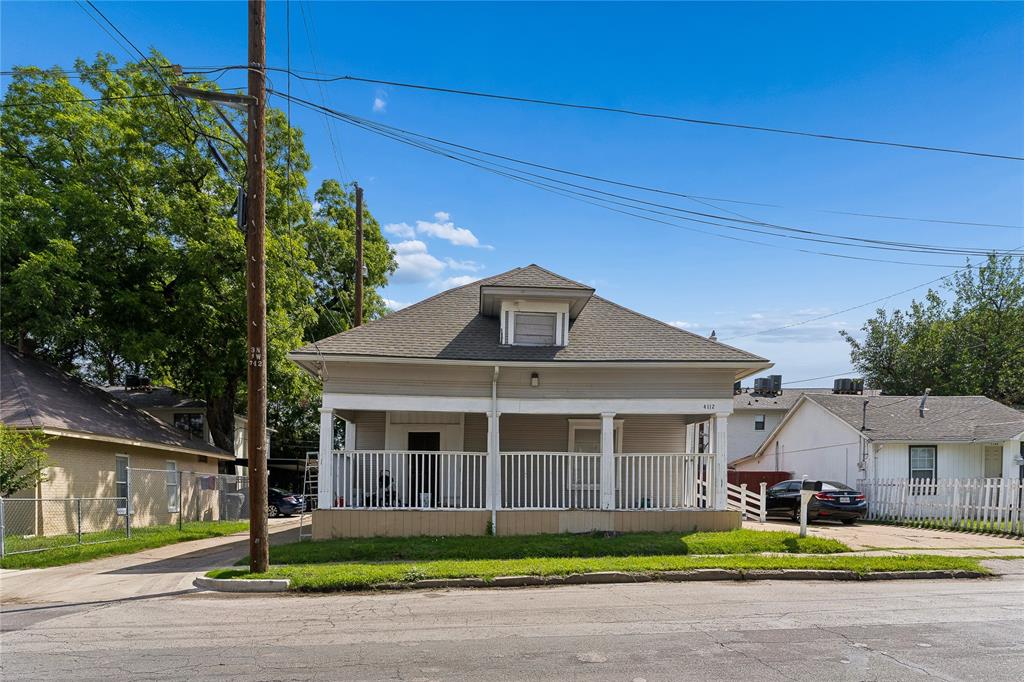 Pitched roof with dormer window, covered porch with white columns and railing, light-colored exterior siding, street-facing grass area, and a paved driveway