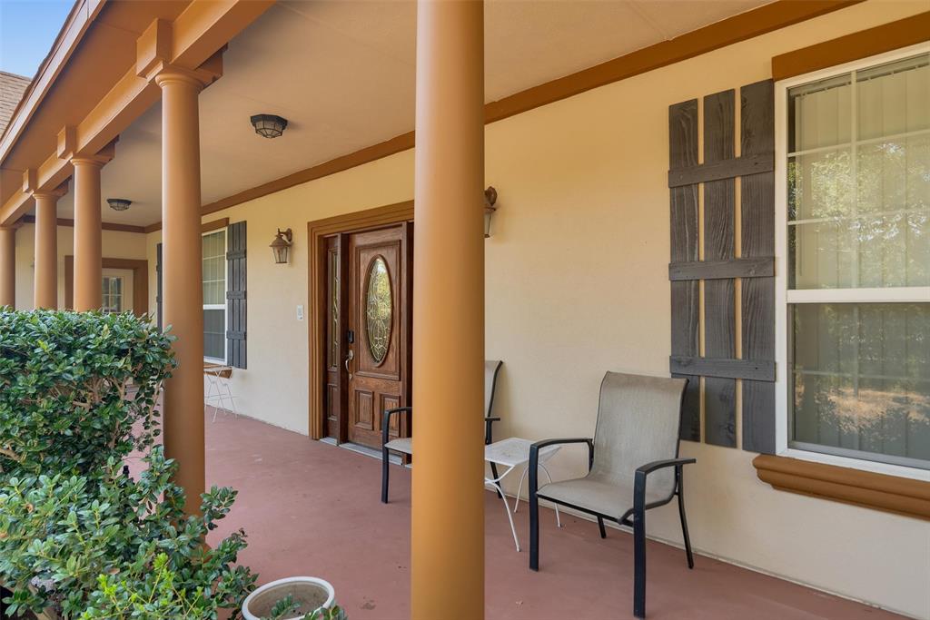 Front porch with multiple columns, wood-finish front door with oval glass insert, exterior wall sconce, and decorative window shutters Front porch with multiple columns, wood-finish front door with oval glass insert, exterior wall sconce, and decorative window shutters