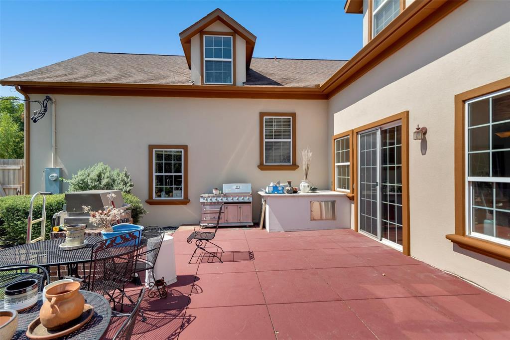 Expansive patio featuring a built-in outdoor kitchen, sliding glass doors, and stucco exterior with brown trim