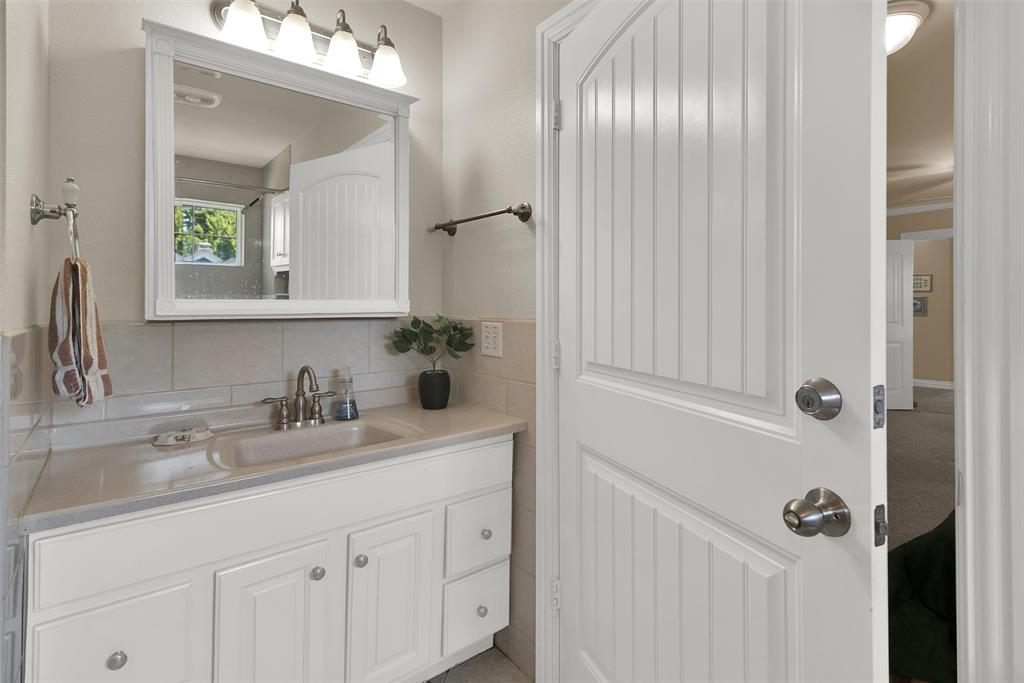 White vanity with an integrated sink and brushed nickel faucet, framed mirror with overhead lighting, and beadboard interior door