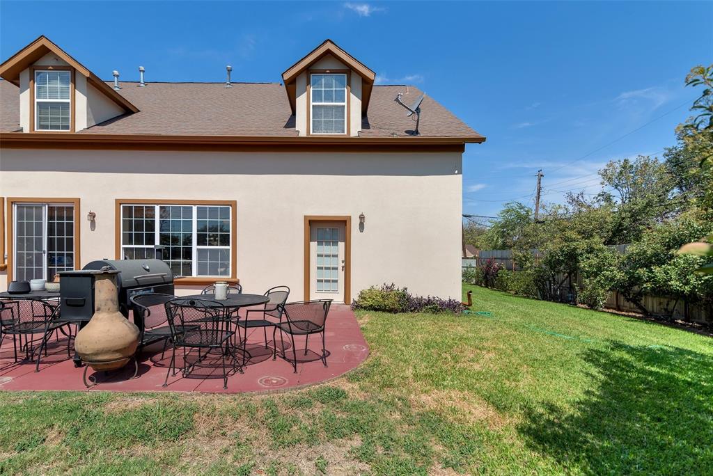 Expansive backyard featuring a red concrete patio, sliding glass door access, multiple windows, a side entry door, and dormer windows on the second level