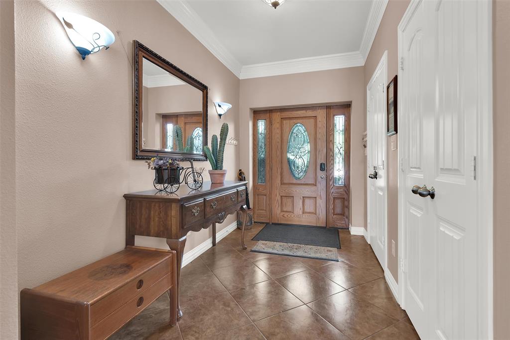 Entryway featuring tile flooring, a wood-paneled door with decorative glass inserts, and crown molding Entryway featuring tile flooring, a wood-paneled door with decorative glass inserts, and crown molding