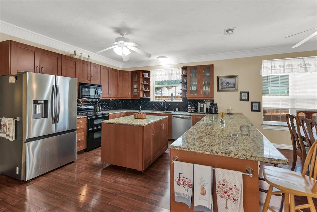 Kitchen featuring wood-finish flooring, stainless steel appliances, granite countertops, wood cabinetry, and a central island