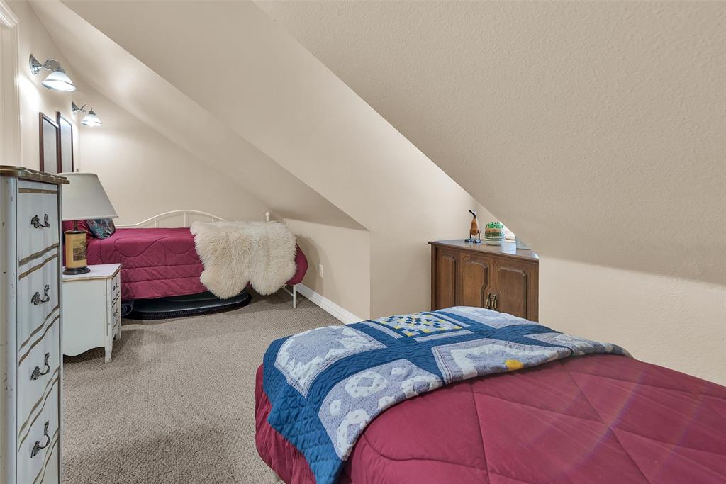 Sloped ceiling room featuring neutral-toned walls, carpet flooring, wall-mounted light fixtures, and a built-in wood-finish cabinet