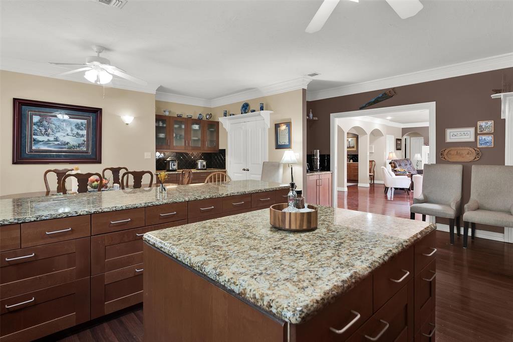 Kitchen featuring two granite-topped islands, rich wood-finish cabinetry, built-in appliances, and hardwood flooring