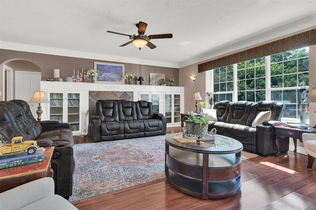 Spacious living area featuring wood-finish flooring, a ceiling fan, crown molding, and a large window wall Spacious living area featuring wood-finish flooring, a ceiling fan, crown molding, and a large window wall