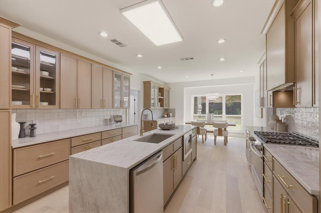 Gourmet kitchen with light wood-finish cabinetry, stone countertops, stainless steel appliances, and a central island with an undermount sink