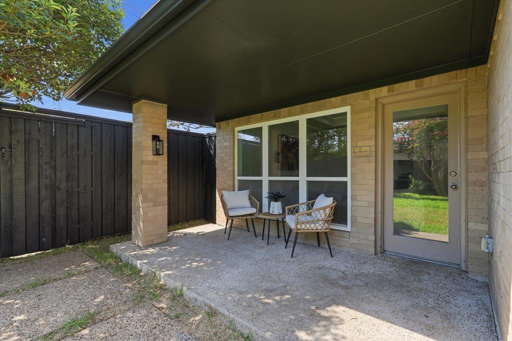 Covered patio with a concrete surface, brick column, and black privacy fence