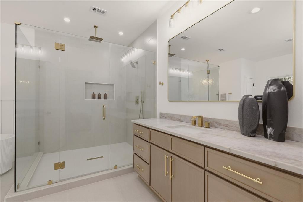 Expansive walk-in shower with a glass enclosure, built-in recessed shelf, and gold-finish fixtures