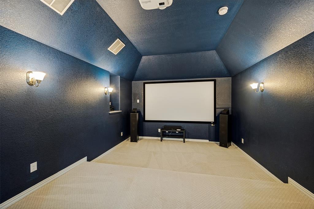 Media room with sloped ceiling, built-in projector screen, and sconce lighting