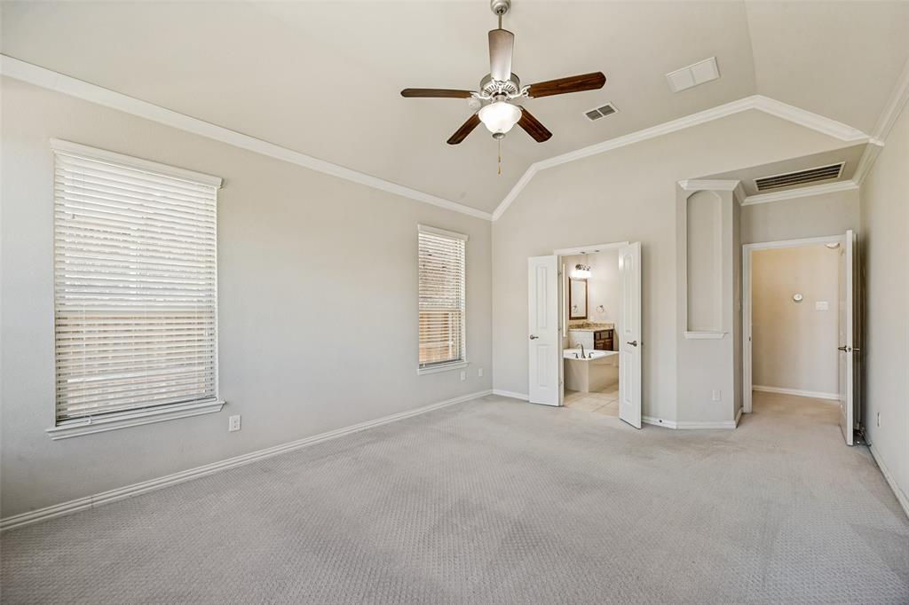 Vaulted ceiling with crown molding, two windows with blinds, a ceiling fan with light fixture, and carpeted flooring