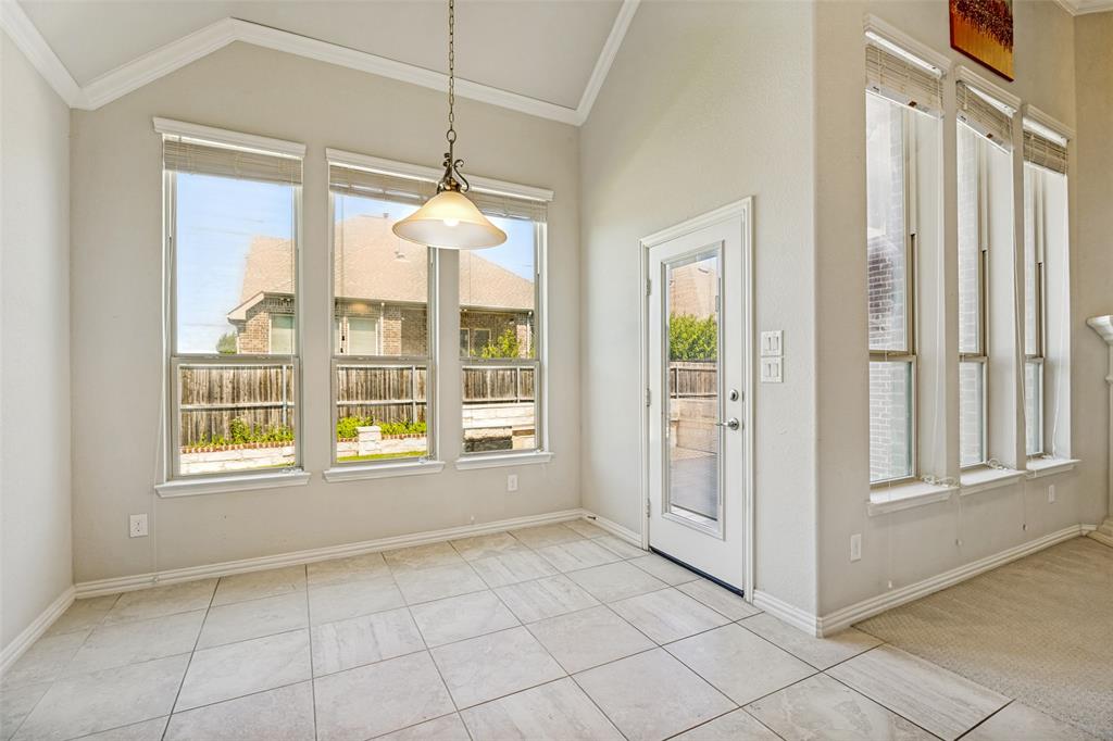 Vaulted ceiling with crown molding, ceramic tile flooring, multiple windows, a glass-paneled exterior door, and a decorative pendant light fixture