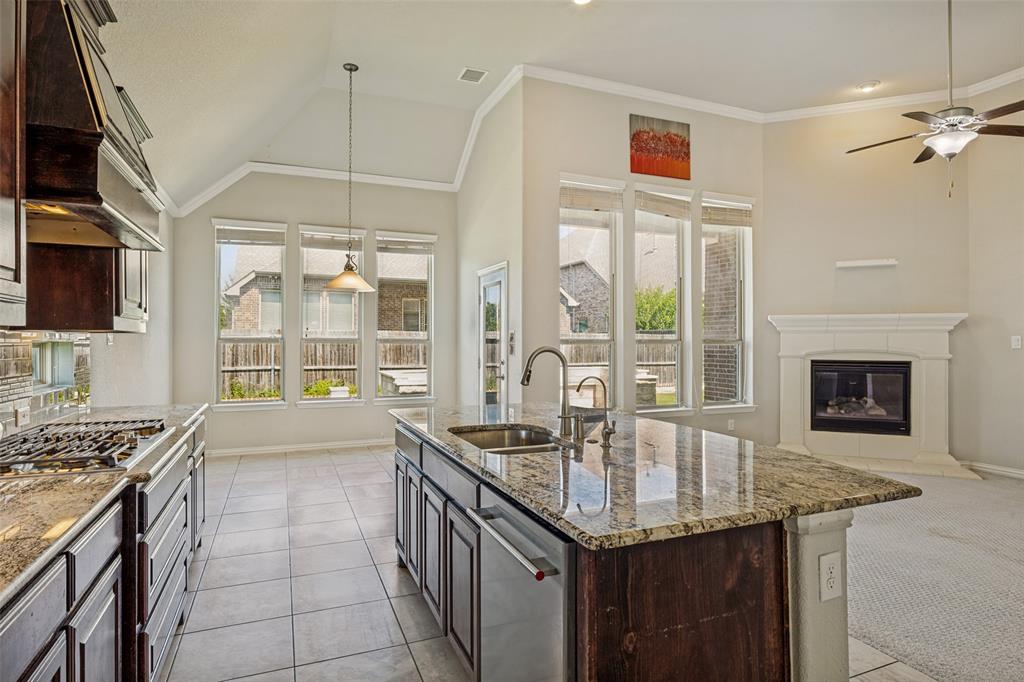 Kitchen island with an undermount sink, granite countertops, tile flooring, gas range, and a fireplace with a mantel