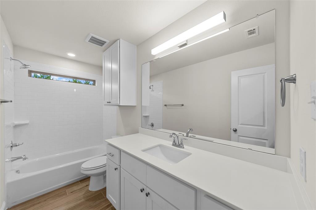 White subway tile tub surround, elongated vanity mirror, white cabinetry, wood-finish flooring, and white solid surface countertop