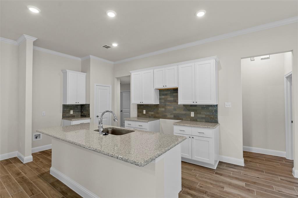 Kitchen featuring a center island with sink, granite-style countertops, white cabinetry, a tiled backsplash, and wood-finish flooring