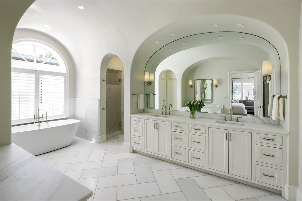 Primary bathroom with dual vanities, stand alone tub, and dual large walk-in closets