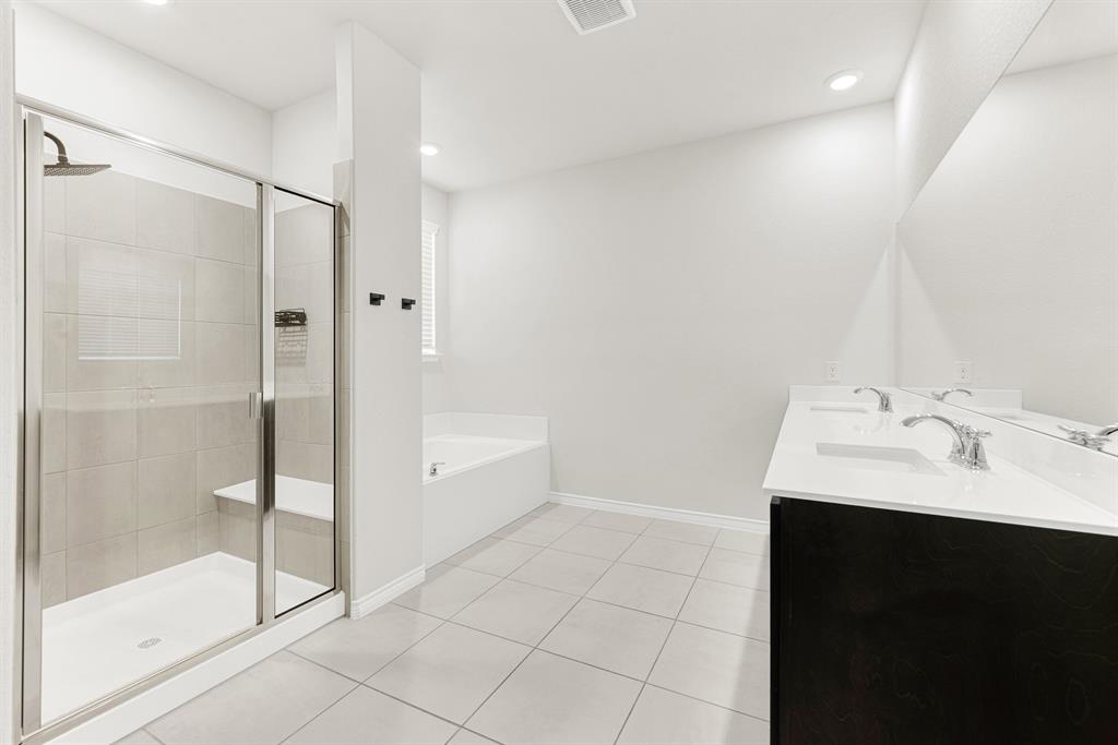 The spacious primary ensuite is revealed in this photo, highlighting the long double-sink vanity with dark cabinetry, large mirror, and separate glass-enclosed tile shower. Start your mornings refreshed or prepare for the day side-by-side in this thoughtfully designed, upscale spa bathroom.