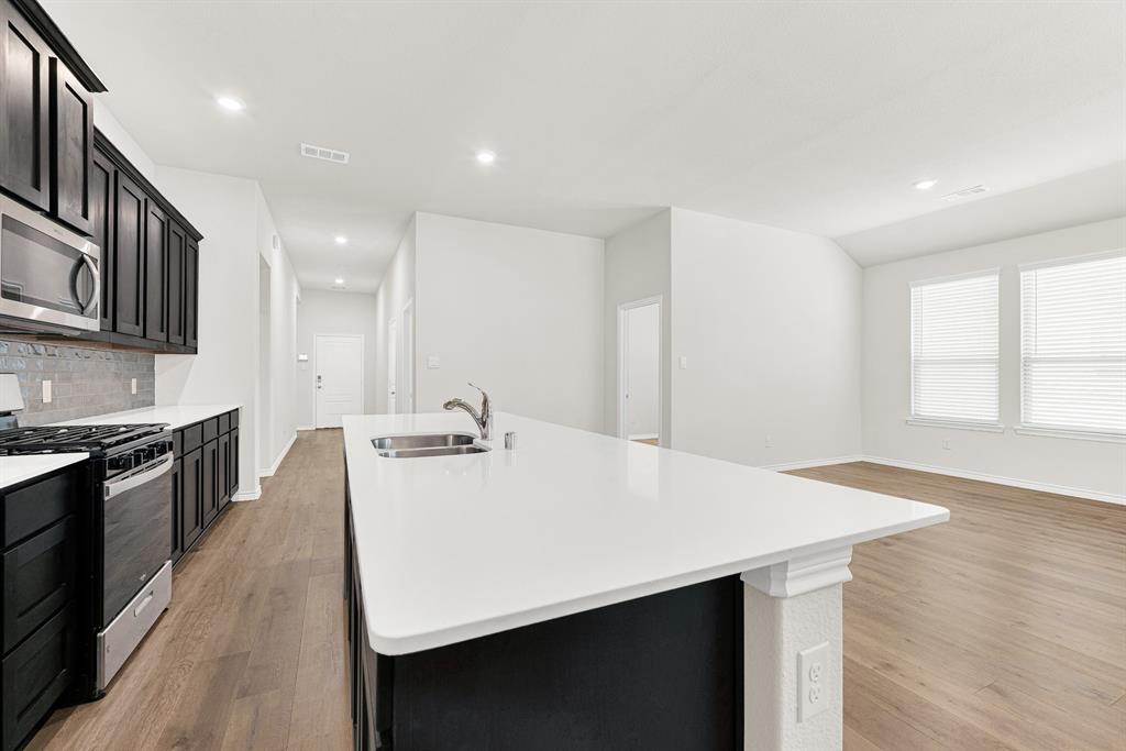 This kitchen's prominent white island features a seamless quartz countertop with an under-mount sink and a gooseneck faucet. You can easily prep meals while staying connected to your family or guests in the open living space This kitchen's prominent white island features a seamless quartz countertop with an under-mount sink and a gooseneck faucet. You can easily prep meals while staying connected to your family or guests in the open living space