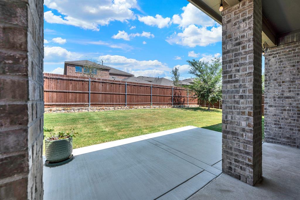 Looking outward from the concrete patio, this angle reveals the expansive green yard, privacy fencing, and stone retaining wall. You will love hosting casual weekend cookouts with plenty of room for kids and pets to play safely.