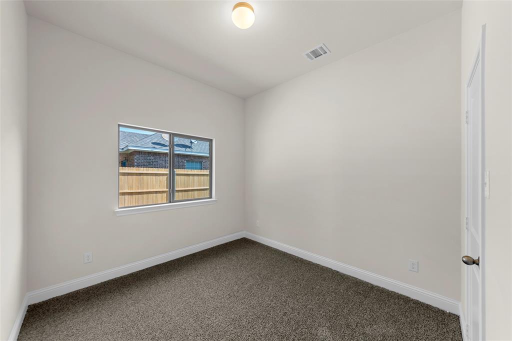 Neutral wall paint, textured carpet flooring, window with exterior fencing, white trim, and a ceiling-mounted light fixture