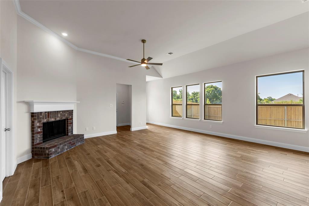 Vaulted ceilings with crown molding, brick fireplace with white mantel, wood-finish flooring, and multiple windows