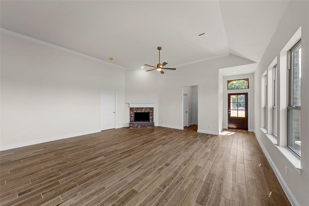 Spacious living area featuring wood-finish flooring, a vaulted ceiling, and a brick fireplace