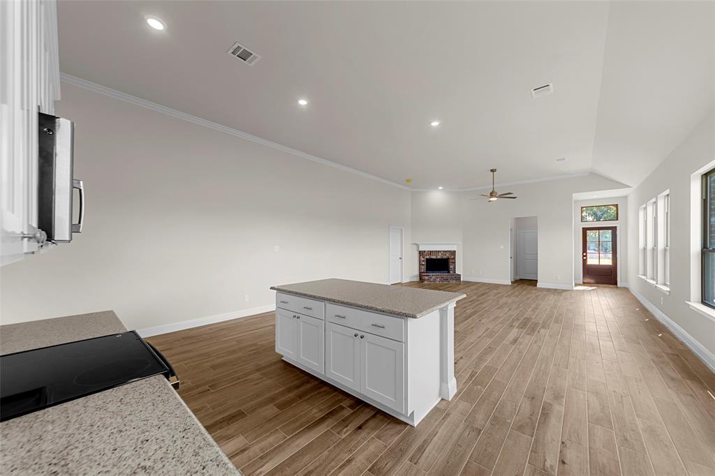Open-concept living space with vaulted ceilings, recessed lighting, wood-finish flooring, stone fireplace, and a kitchen island with stone countertops