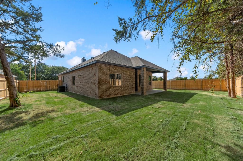 Expansive backyard with a manicured lawn, brick exterior, covered patio, and wood privacy fencing