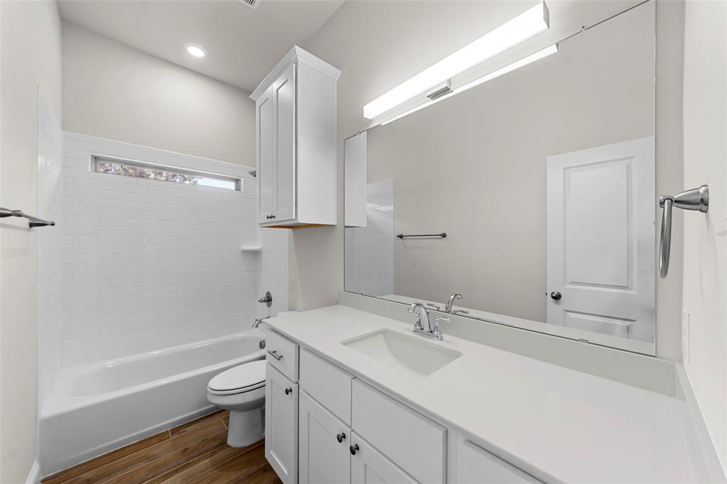 Bathroom featuring a white subway tile tub surround, wood-finish flooring, a single vanity with stone countertop, and recessed lighting