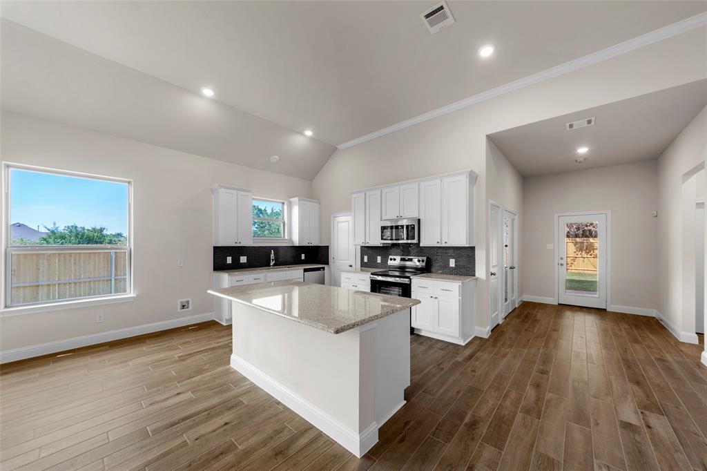 Vaulted ceiling, recessed lighting, wood-finish flooring, white cabinetry, and a kitchen island with a stone countertop