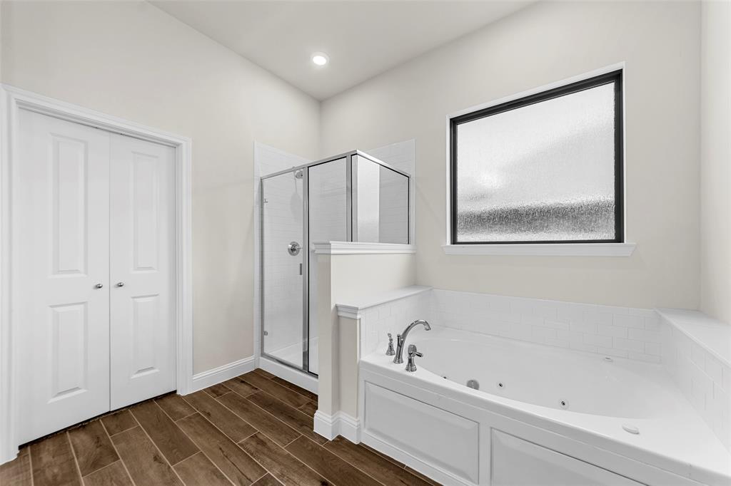 Jetted soaking tub with a tiled surround, glass-enclosed shower, wood-finish flooring, and a privacy window