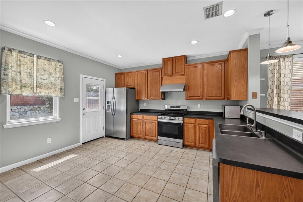 Kitchen featuring wood cabinetry, stainless steel appliances, dark countertops, a double basin sink with a gooseneck faucet, and tile flooring