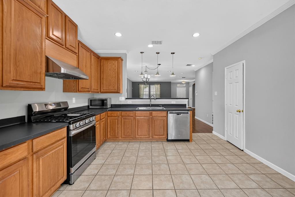 Kitchen featuring wood cabinetry, stainless steel appliances, dark countertops, and tile flooring