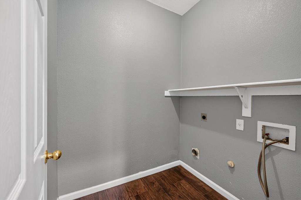 Utility area featuring wood-finish flooring, a white paneled door, and a built-in wall shelf