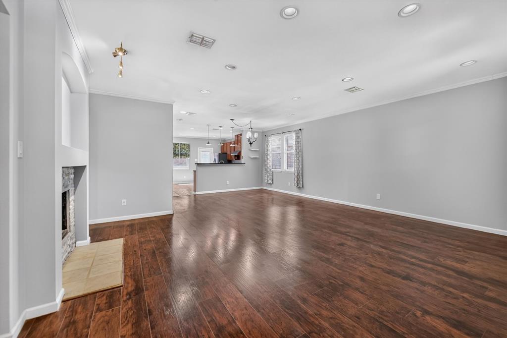 Wood-finish flooring throughout, recessed ceiling lighting, a stone-clad fireplace with a hearth, and crown molding