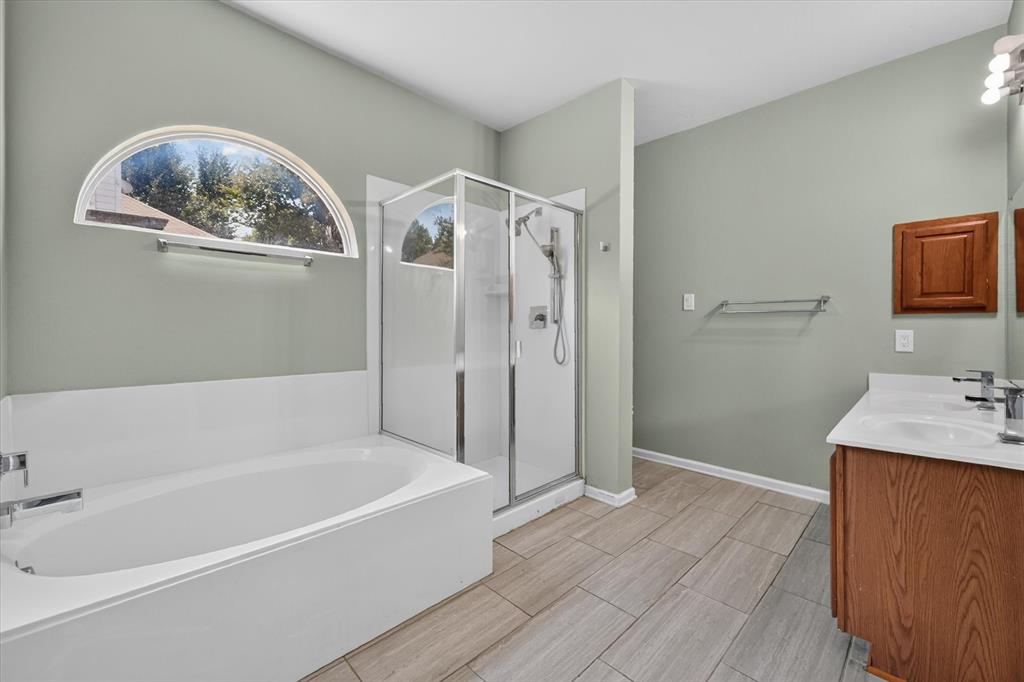Alcove bathtub with an arched window, glass-enclosed shower, dual vanity with undermount sinks, and tile flooring