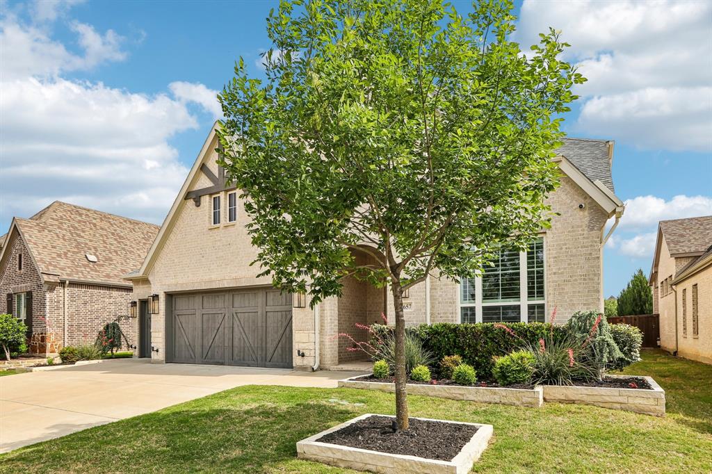 Brick exterior with stone accents, gable roofline, decorative garage door, and established landscaping