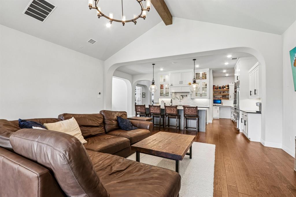 Vaulted ceiling with an exposed beam, hardwood flooring, recessed lighting, arched doorways, and a kitchen featuring white cabinetry