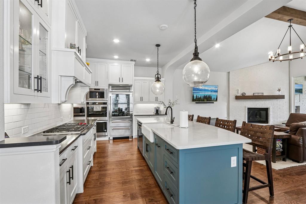 Gourmet kitchen featuring a white subway tile backsplash, stainless steel appliances, a large center island with a farm sink, and wood-finish flooring Gourmet kitchen featuring a white subway tile backsplash, stainless steel appliances, a large center island with a farm sink, and wood-finish flooring