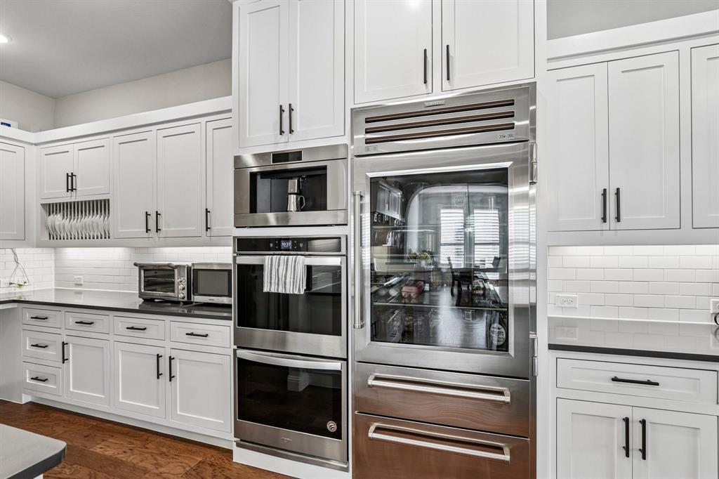 White shaker-style cabinetry with matte black hardware, integrated stainless steel appliances, dark countertops, white subway tile backsplash, and wood-finish flooring White shaker-style cabinetry with matte black hardware, integrated stainless steel appliances, dark countertops, white subway tile backsplash, and wood-finish flooring