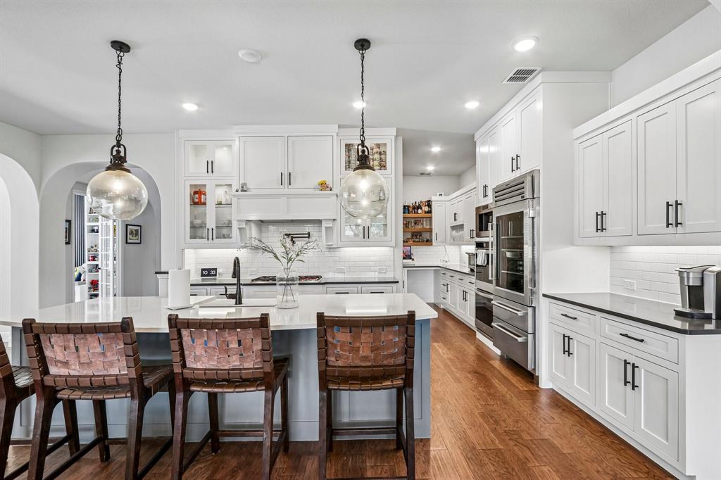 Spacious kitchen featuring white cabinetry, stainless steel appliances, a large center island, wood-finish flooring, and subway tile backsplash Spacious kitchen featuring white cabinetry, stainless steel appliances, a large center island, wood-finish flooring, and subway tile backsplash